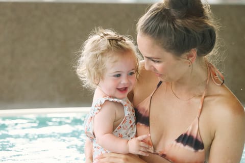 Mama hält ihr Kleinkind im Arm im warmen Wasser des Hallenbads