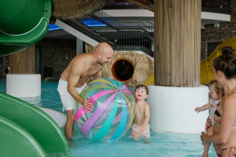 Papa spielt mit Kleinkindern und einem großen Wasserball im Kinderbecken