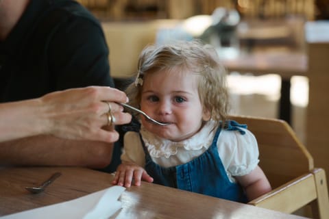 Kleinkind im Hochstuhl wird im Restaurant mit dem Löffel gefüttert